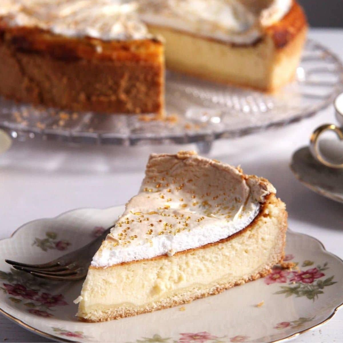 a slice of authentic german cheesecake on a vintage plate, the rest of the cake behind it.