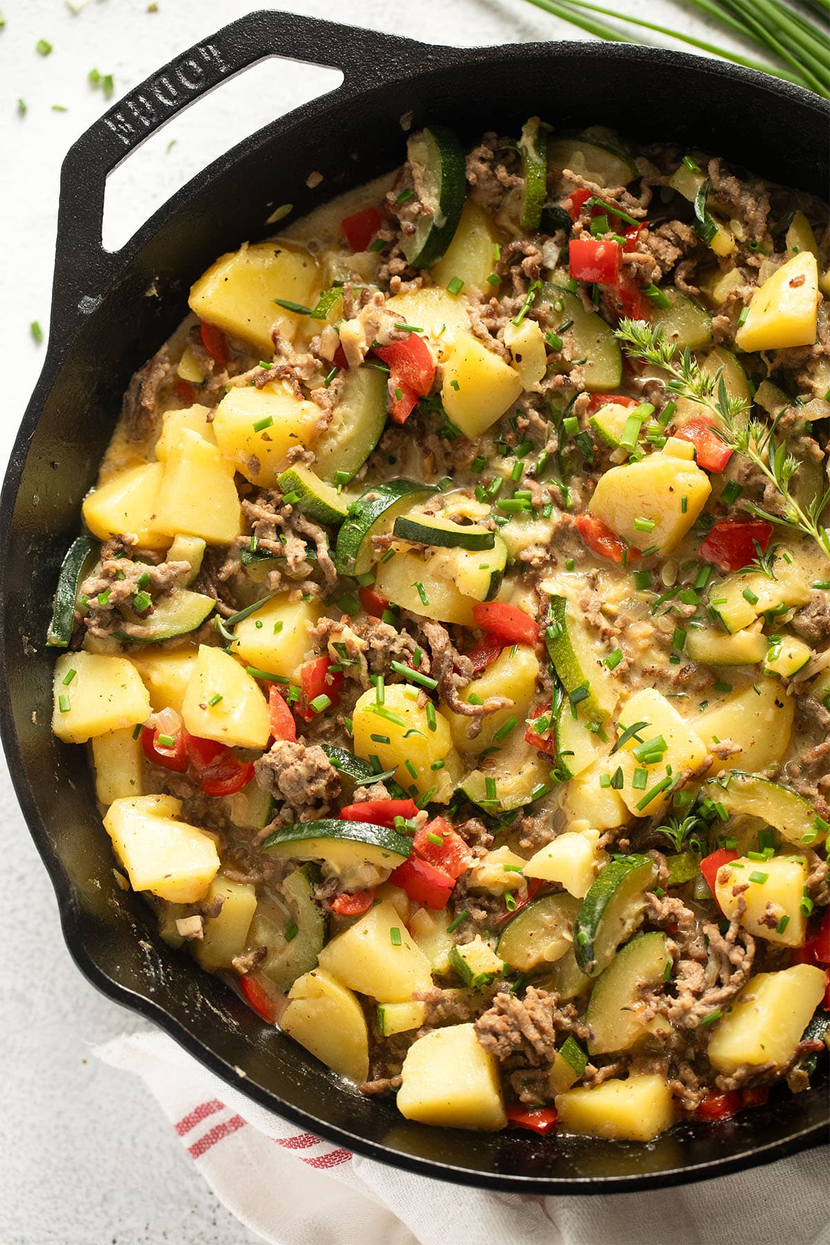 skillet full of ground beef, potatoes and zucchini sprinkled with herbs.