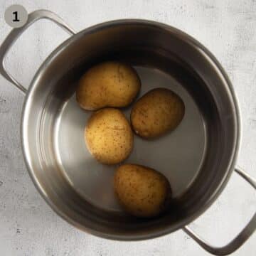 four small potatoes cooking in water in a pot.