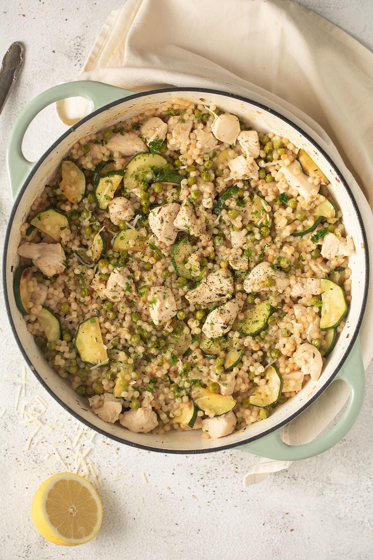 pot full of israeli couscous with chicken pieces, zucchini, and peas.