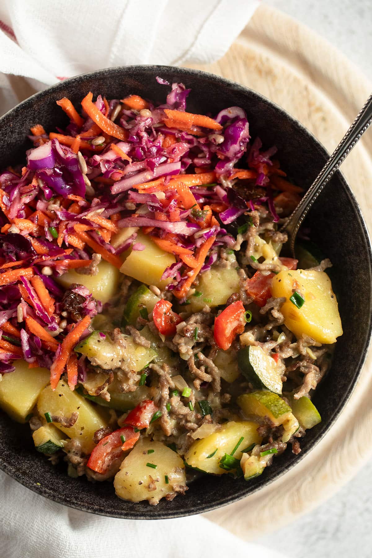 plate with ground beef, potatoes and zucchini served with red cabbage and carrot slaw.