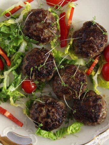 many juicy meatballs and fresh vegetables on a small plate.