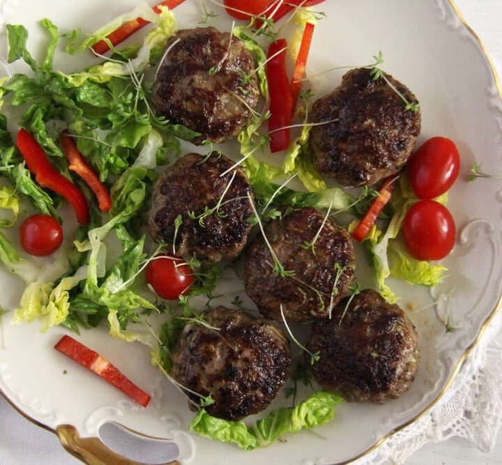 many juicy meatballs and fresh vegetables on a small plate.