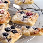 marzipan pastries with puff pastry and berries on a cooling rack