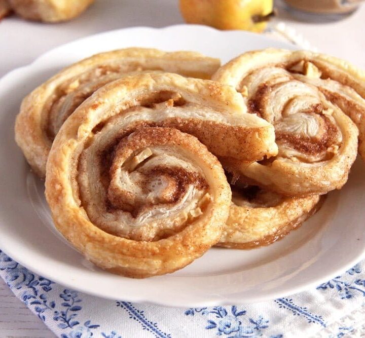 apple puff pastry rolls with cinnamon on a small white plate