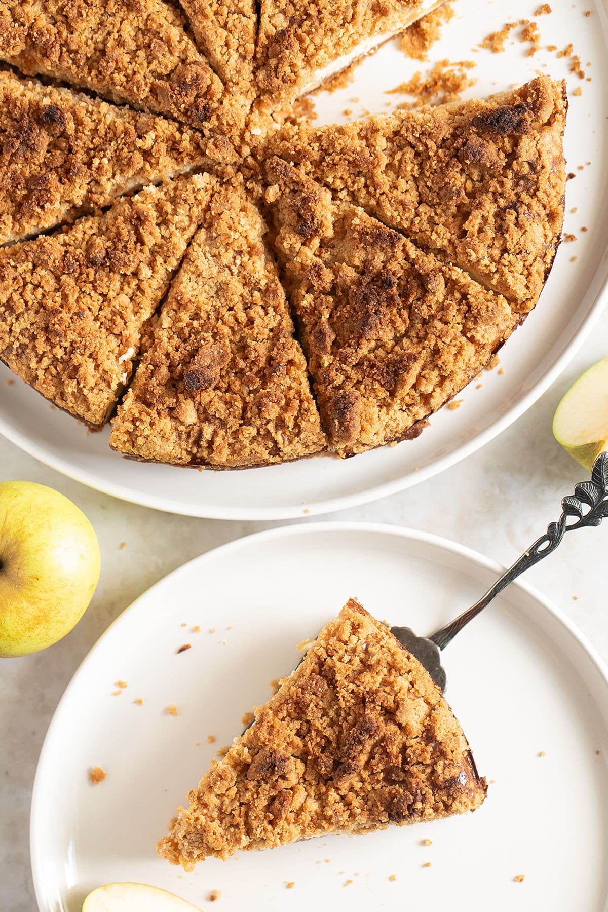 apple streusel cheesecake on a platter and a slice of it on a plate.