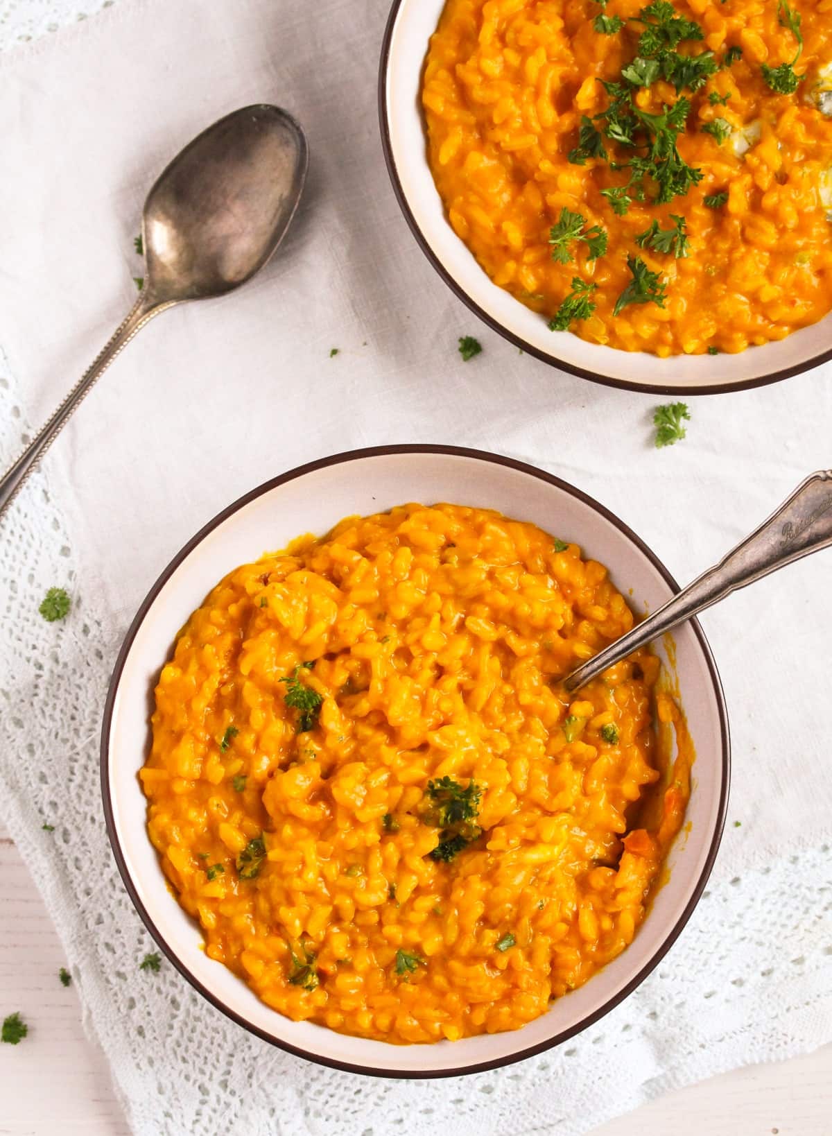 two bowls of gorgonzola risotto with pumpkin, one sprinkled with parsley.