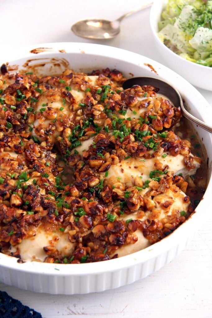 white baking dish with chicken breast topped with roasted hazelnuts