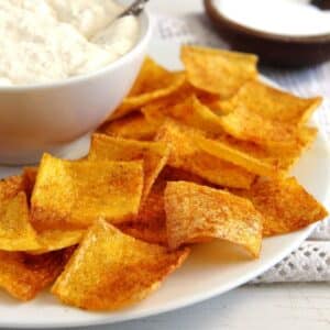 many square and crispy polenta crisps on a plate with a bowl of cream cheese dip.