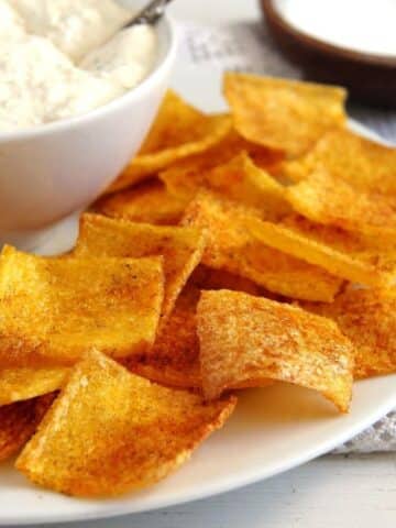 many square and crispy polenta crisps on a plate with a bowl of cream cheese dip.