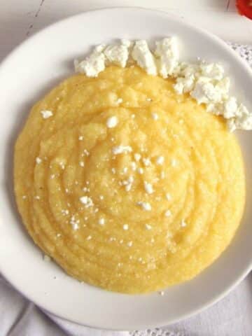 romanian polenta or mamaliga topped with crumbled feta cheese in a bowl.