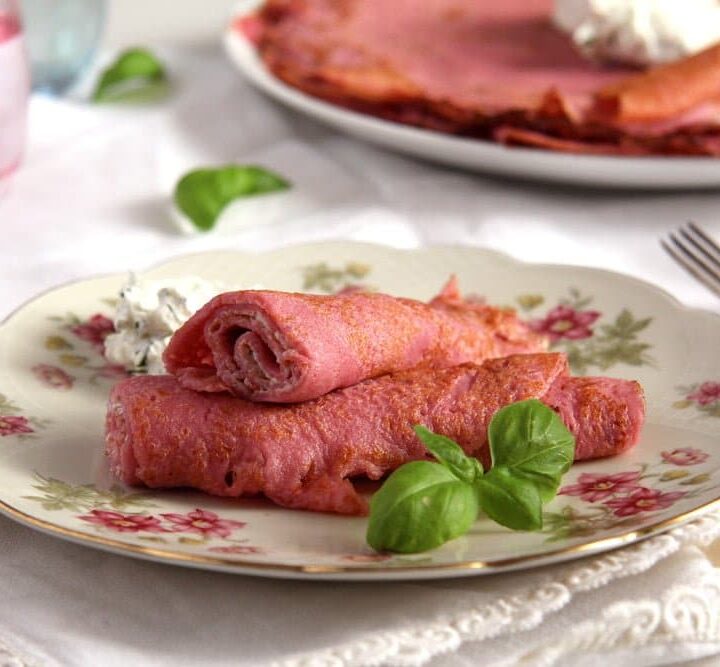 pink beetroot crepes with sweet or savory filling rolled on a plate with basil leaves.