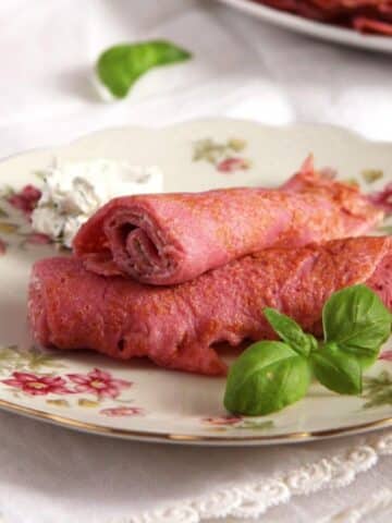 two rolled pink beetroot crepes and fresh basil leaves on a vintage plate.