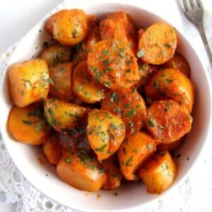 a bowl of potatoes with tomato sauce sprinkled with parsley.