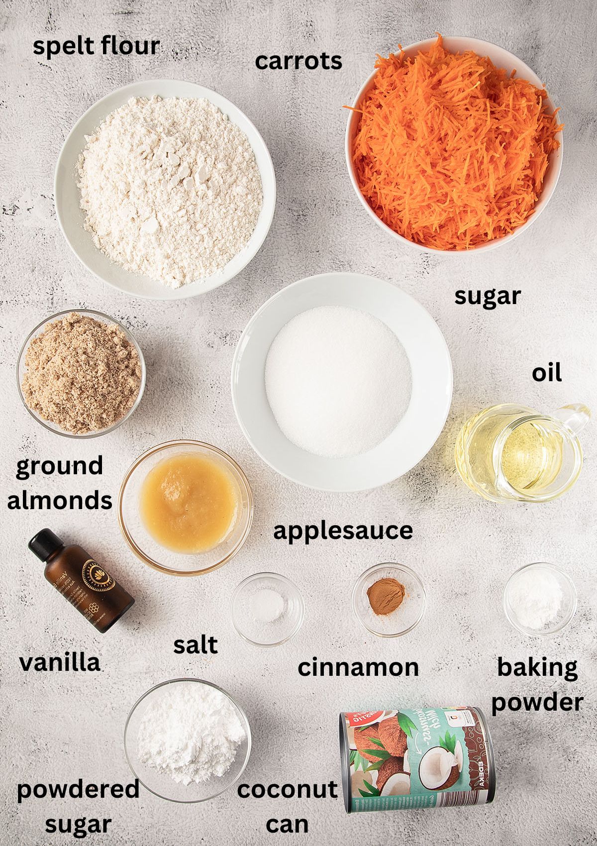 labeled ingredients for making a vegan carrot cake with spelt flour, coconut cream frosting, ground almonds and cinnamon.