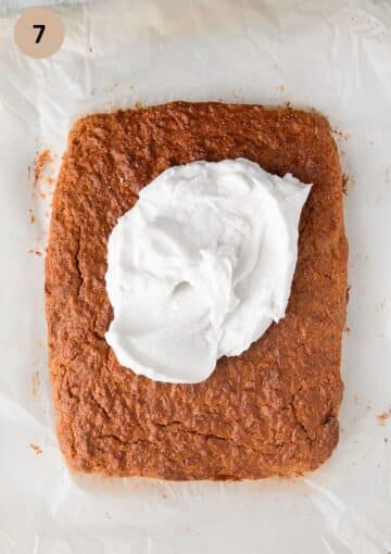 spreading a dollop of coconut cream frosting on a rectangular carrot cake.
