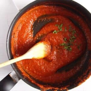 spicy marinara sauce stirred with a wooden spoon in a pot.