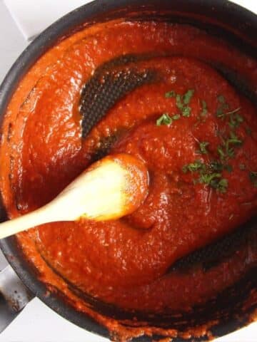 spicy marinara sauce stirred with a wooden spoon in a pot.