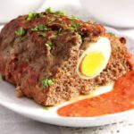 meatloaf with eggs served with tomato sauce on a platter.