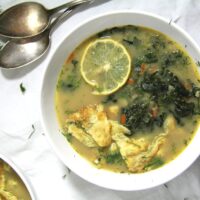 spinach soup with eggs in a white bowl served with lemon slices