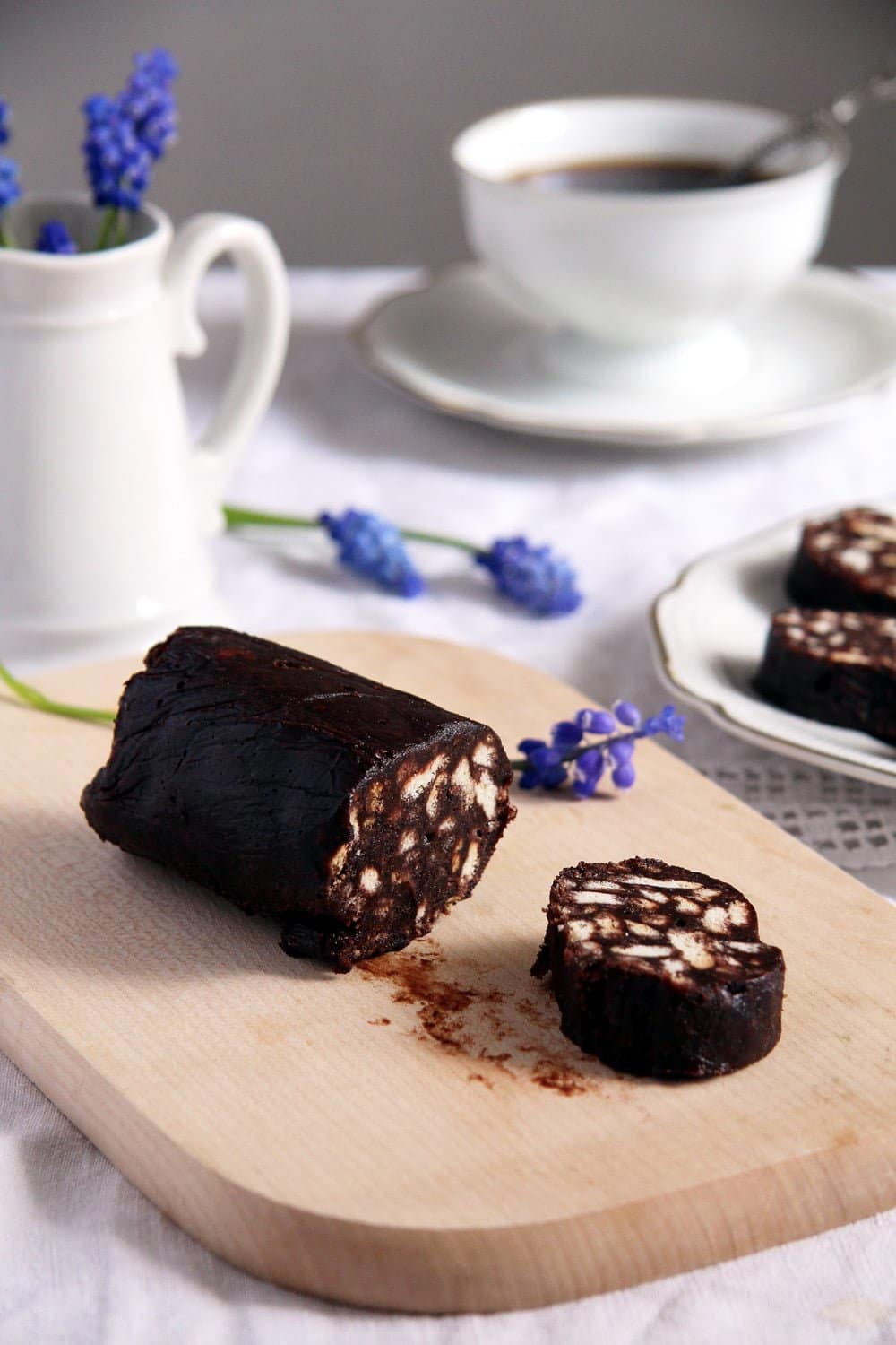 roll of biscuit chocolate salami on a wooden board, a small flower pot behind it.