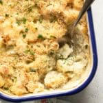 creamy cauliflower in white sauce in a baking dish with a spoon in it.