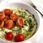 cauliflower potato mash with fried sausage slices in a white bowl