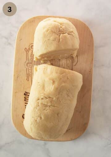 a log of cake dough cut into two uneven parts on a cutting board.