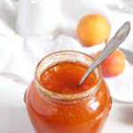 apricot jam in a jar with flowers and apricots behind