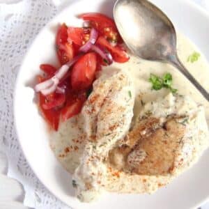 romanian cream chicken served with tomato salad on a small plate with a spoon.