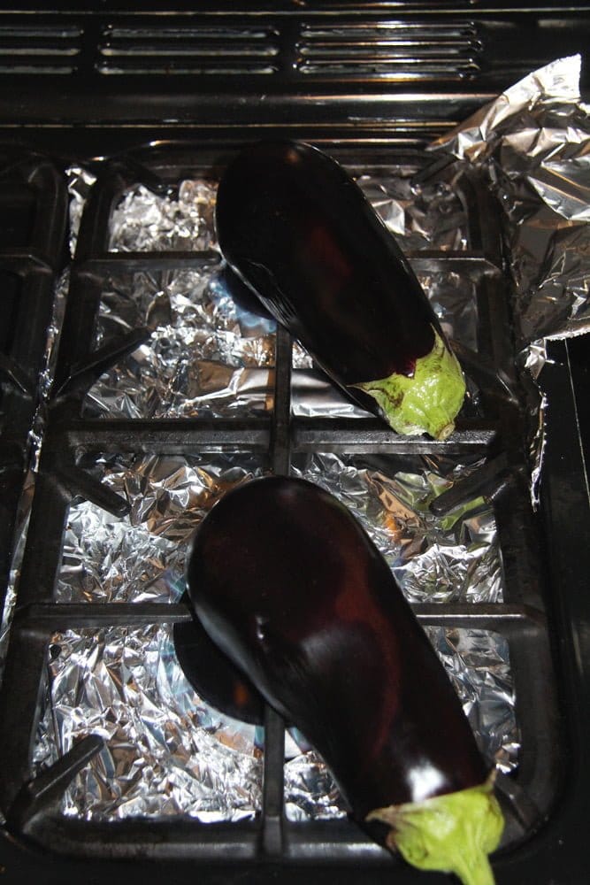 two eggplants being roasted on a stovetop lined with foil.