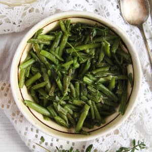 romanian green beans with garlic sauce in a traditional bowl with a spoon beside it.