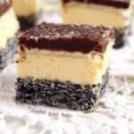 three layered square or chocolate poppy seed cake with vanilla buttercream and chocolate on top.