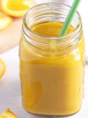 apple turmeric smoothie in a jar with a green straw in it.