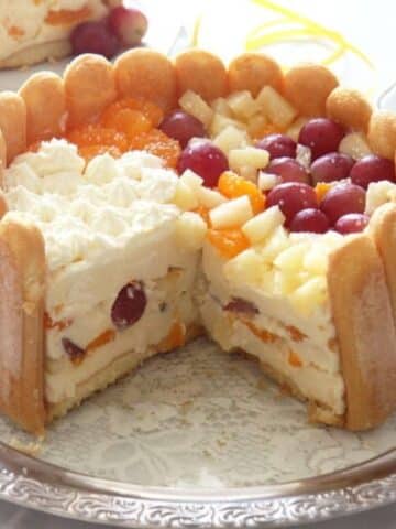 romanian diplomat cake with ladyfingers and fruit cut on a platter showing the insides.