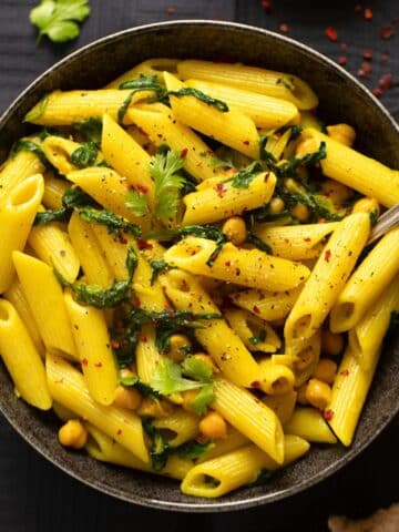 turmeric pasta in a dark bowl with a fork in it.