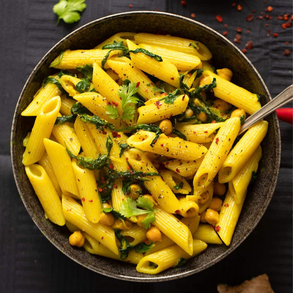 turmeric pasta in a dark bowl with a fork in it.