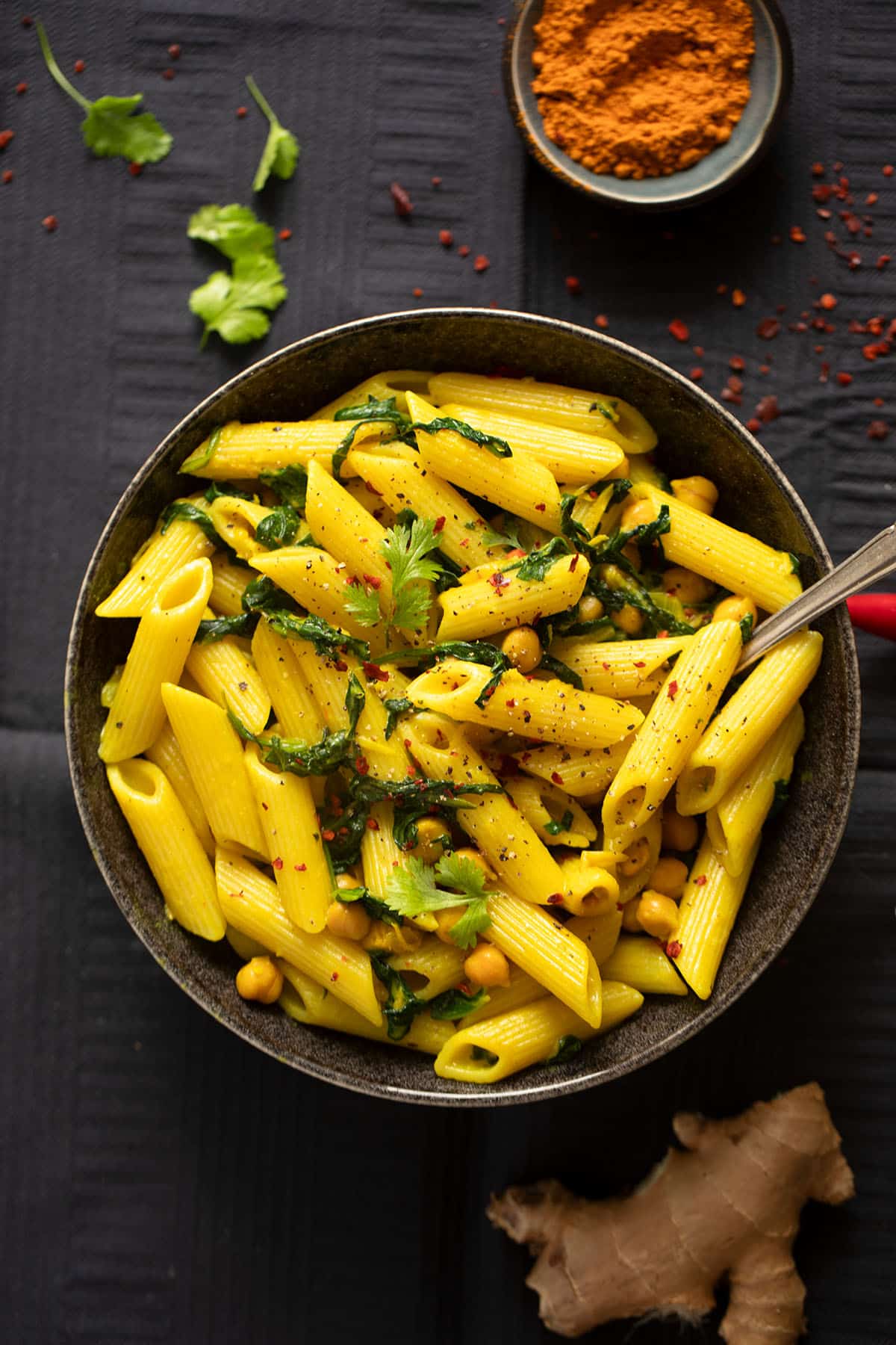 bowls of turmeric pasta and ground turmeric, cilantro and a piece of ginger around it.