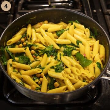 combining penne with golden turmeric sauce and spinach in a saucepan.