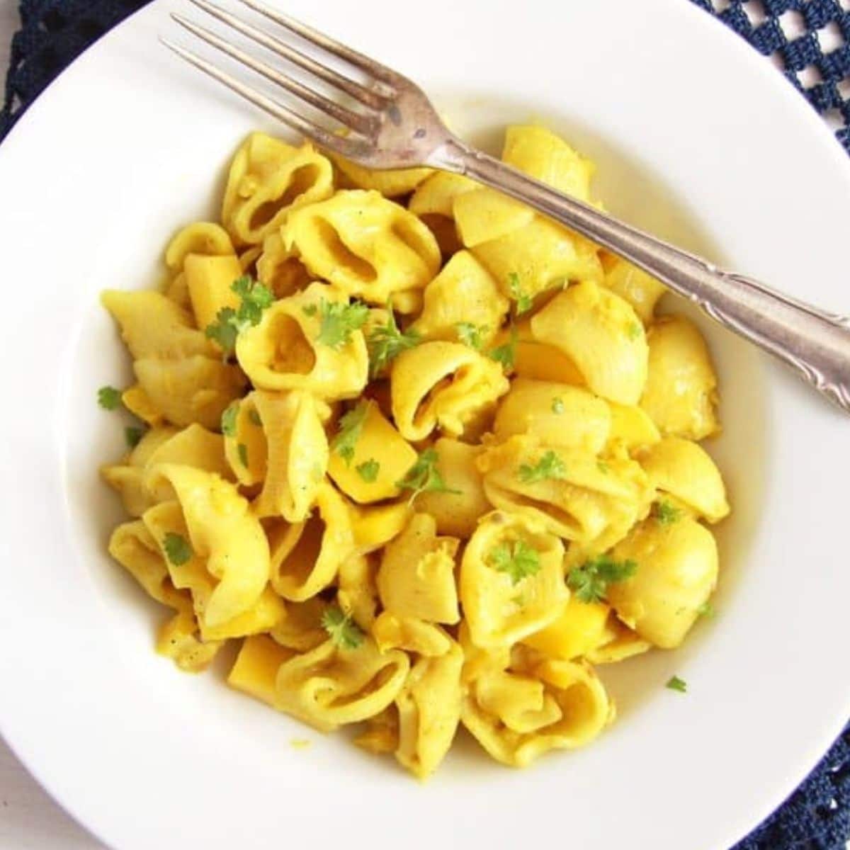 yellow colored turmeric pasta with a fork in a white plate.
