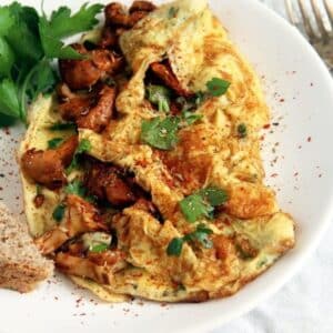 close up of fluffy chanterelle omelet with parsley on a white plate.