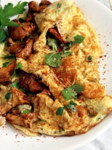 close up of fluffy chanterelle omelet with parsley on a white plate.