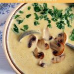 pinterest image of cream of mushroom soup decorated with sauteed mushrooms and parsley.
