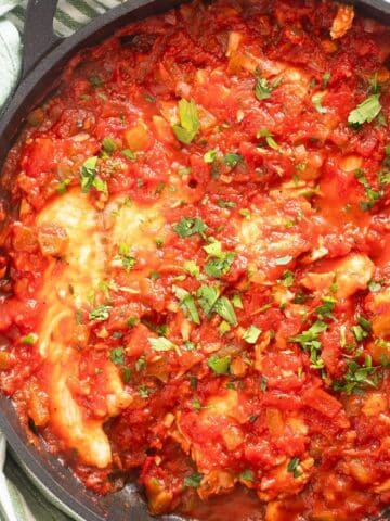 white fish in tomato sauce and sprinkled with parsley in a large skillet.