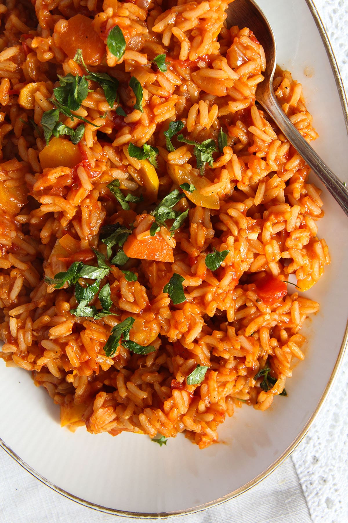 tomato and zucchini rice sprinkled with parsley on a platter with a spoon.