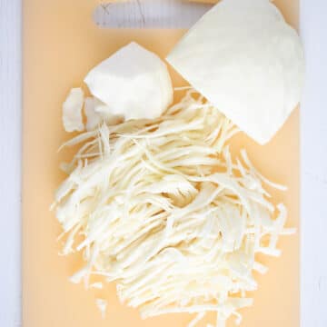 pieces of white cabbage and some shredded on a cutting board.