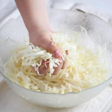 a hand squeezing shredded salad in a bowl to soften it.