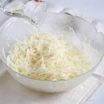 pouring oil over shredded cabbage in a bowl.