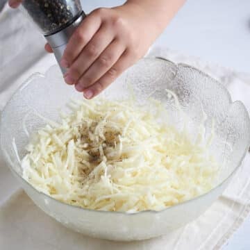 kid's hands sprinkling pepper in a bowl of cabbage salad.