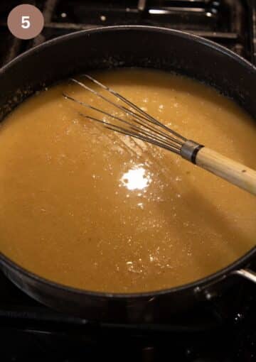 whisking white sauce with a hand whisk in a pan.
